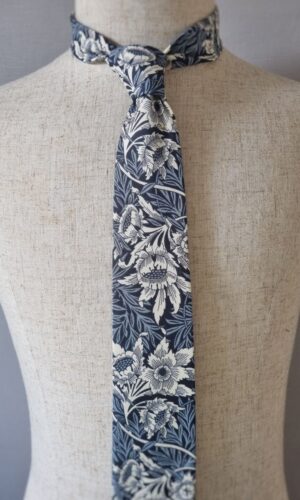 Experience the timeless elegance of the "Tulip and Willow William Morris Tie," a tribute to the rich history of design by William Morris. This exquisite accessory features a sophisticated combination of navy and inky blue, adorned with delicate ivory florals. Drawing inspiration from the intricate artwork of William Morris, the "Tulip and Willow" pattern holds a special place in the history of textile design. Originally created as a watercolour masterpiece, the pattern took years to be successfully produced for commercial use. Morris's quest for perfection led him to collaborate with Thomas Wardle at his print works in Leek, Staffordshire in 1875. Together, they experimented with natural dyes, striving to capture the true essence of Morris's vision. However, it wasn't until 1883 that the pattern was successfully achieved using the indigo discharge method in Morris's own factory at Merton Abbey, Wimbledon. Wearing the "Tulip and Willow William Morris Tie" is not only an expression of style but also a nod to the enduring spirit of artistic perseverance. Each intricate detail showcases the craftsmanship and dedication that went into its creation. Embrace the legacy of William Morris and his pursuit of beauty as you adorn yourself with this remarkable tie. Let it become a conversation piece, inviting others to appreciate the artistry and historical significance it represents. Carry a piece of history with you and revel in the timeless charm of the "Tulip and Willow William Morris Tie."