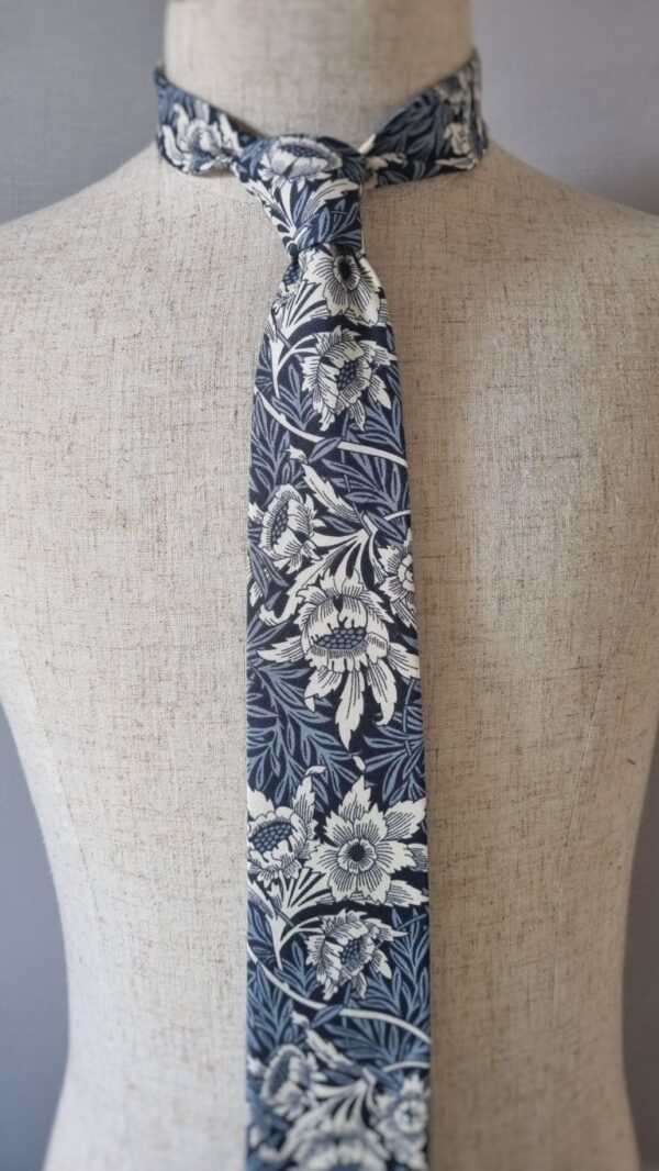 Experience the timeless elegance of the "Tulip and Willow William Morris Tie," a tribute to the rich history of design by William Morris. This exquisite accessory features a sophisticated combination of navy and inky blue, adorned with delicate ivory florals. Drawing inspiration from the intricate artwork of William Morris, the "Tulip and Willow" pattern holds a special place in the history of textile design. Originally created as a watercolour masterpiece, the pattern took years to be successfully produced for commercial use. Morris's quest for perfection led him to collaborate with Thomas Wardle at his print works in Leek, Staffordshire in 1875. Together, they experimented with natural dyes, striving to capture the true essence of Morris's vision. However, it wasn't until 1883 that the pattern was successfully achieved using the indigo discharge method in Morris's own factory at Merton Abbey, Wimbledon. Wearing the "Tulip and Willow William Morris Tie" is not only an expression of style but also a nod to the enduring spirit of artistic perseverance. Each intricate detail showcases the craftsmanship and dedication that went into its creation. Embrace the legacy of William Morris and his pursuit of beauty as you adorn yourself with this remarkable tie. Let it become a conversation piece, inviting others to appreciate the artistry and historical significance it represents. Carry a piece of history with you and revel in the timeless charm of the "Tulip and Willow William Morris Tie."